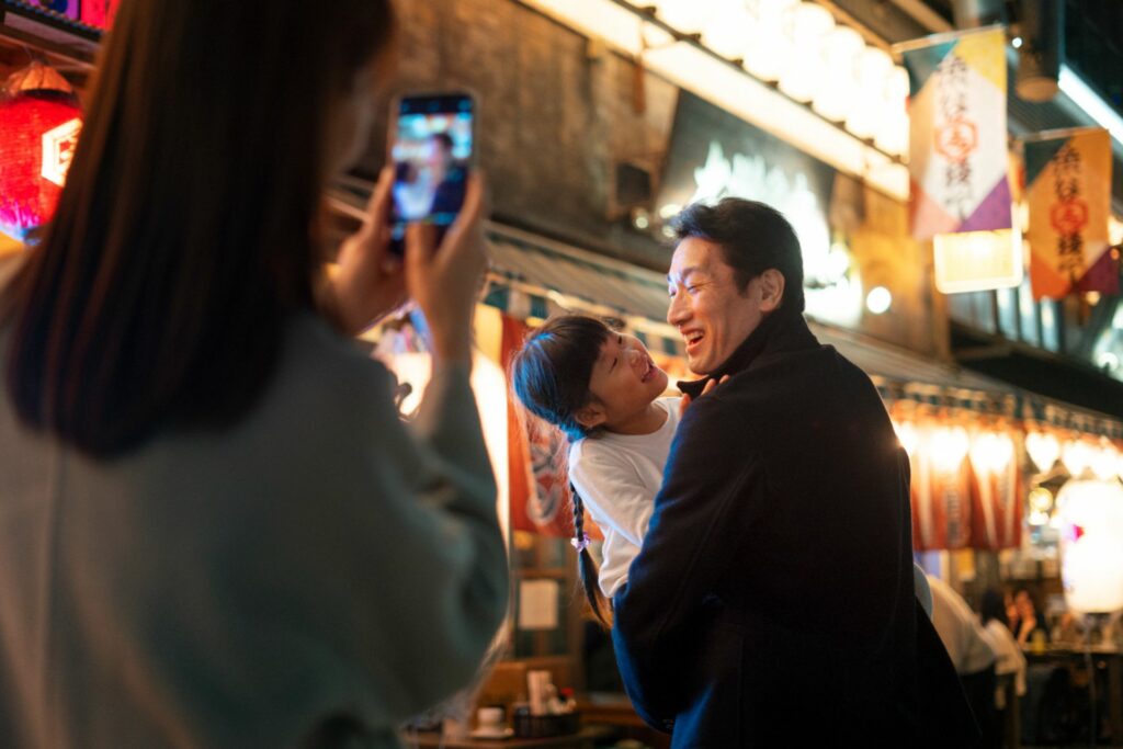 Family taking photos with a phone in a lively Japanese street at night