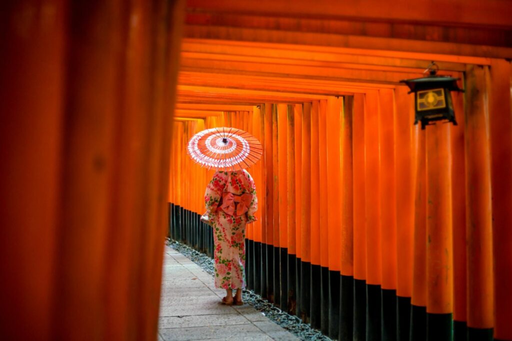 Woman with umbrella walking through torii gates